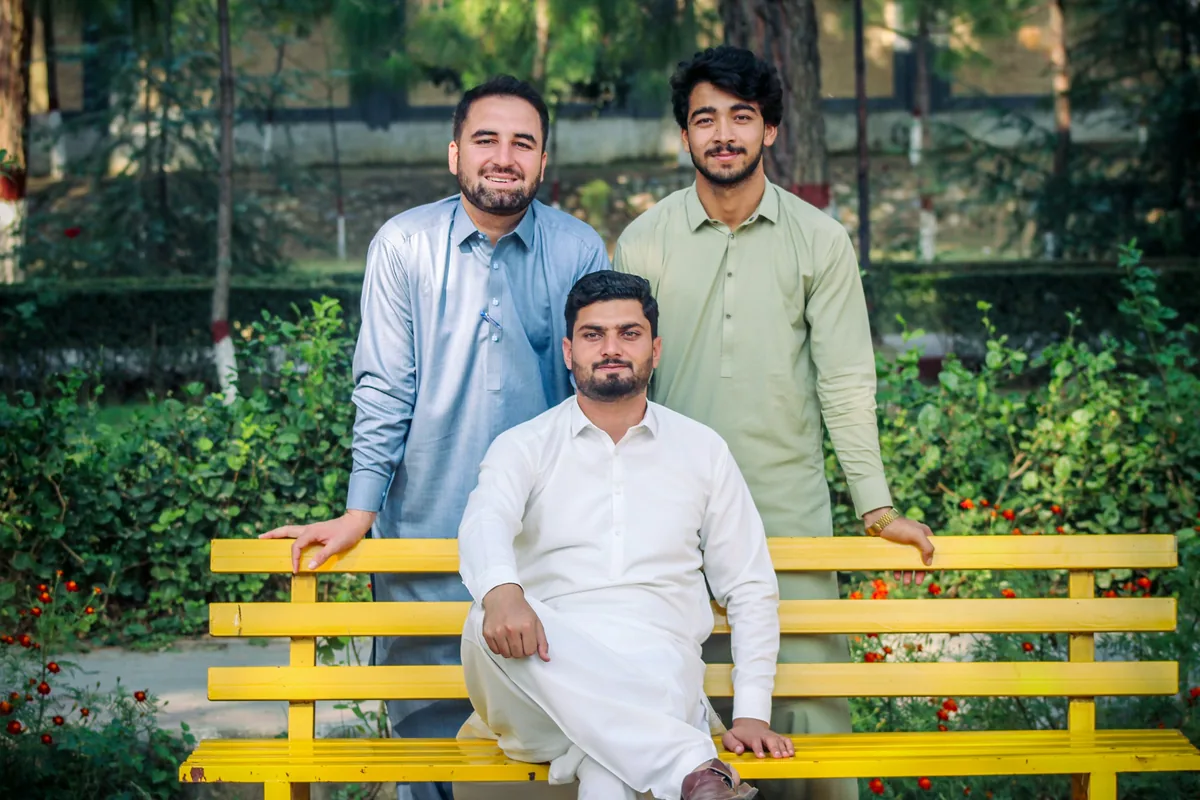 Three friends in shalwar kameez smiling together on a yellow park bench