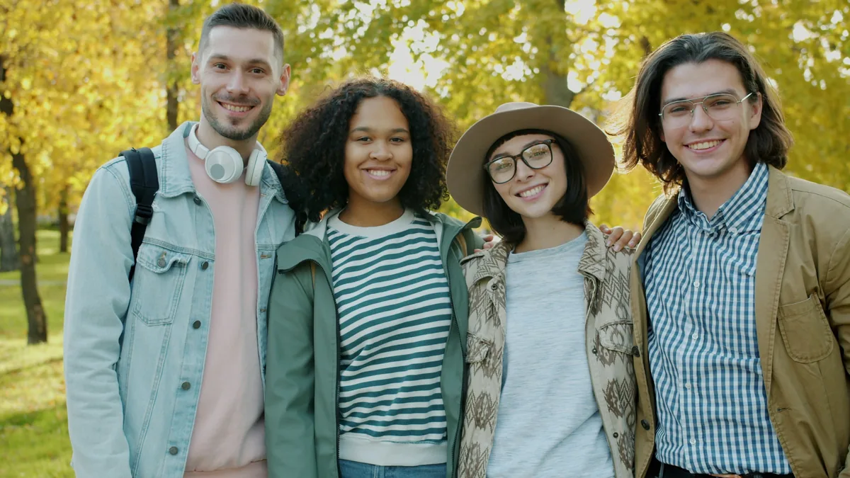 Four young friends from different backgrounds smiling together in an autumn park