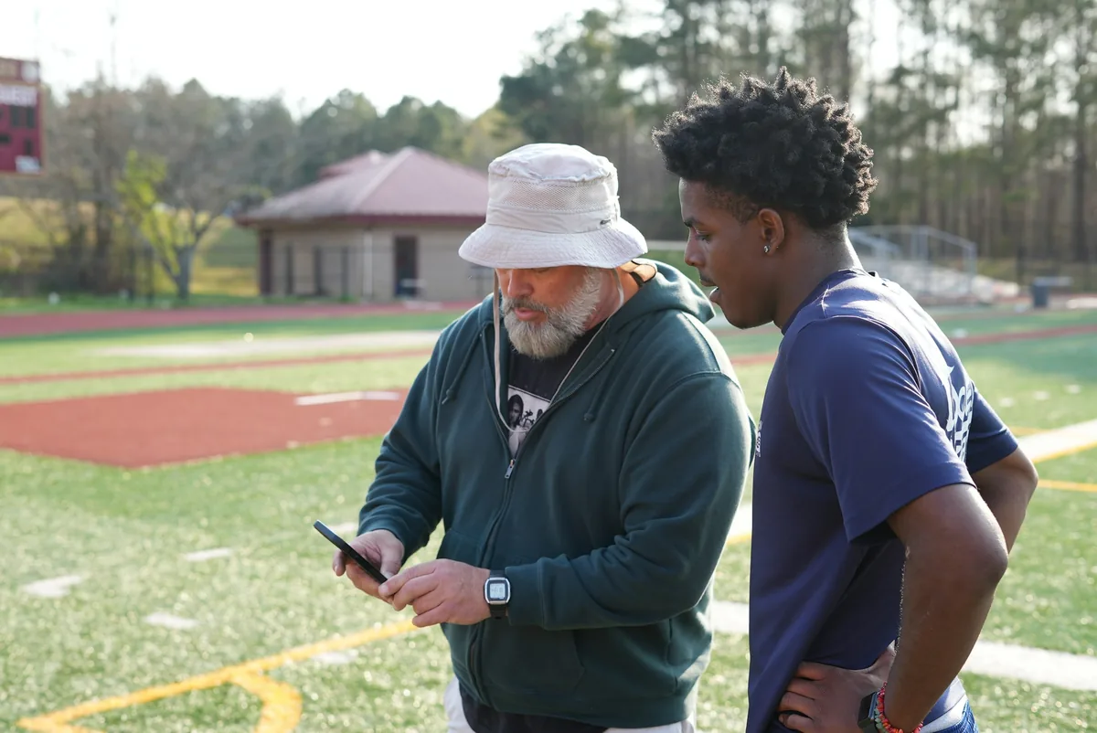 A coach and a young player talking quietly on the sideline of a sports field
