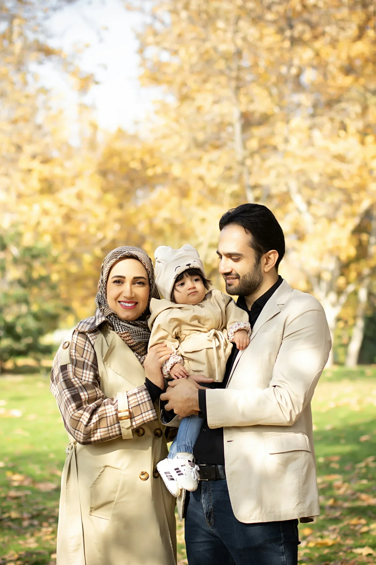 A mother and father holding their young child among autumn trees