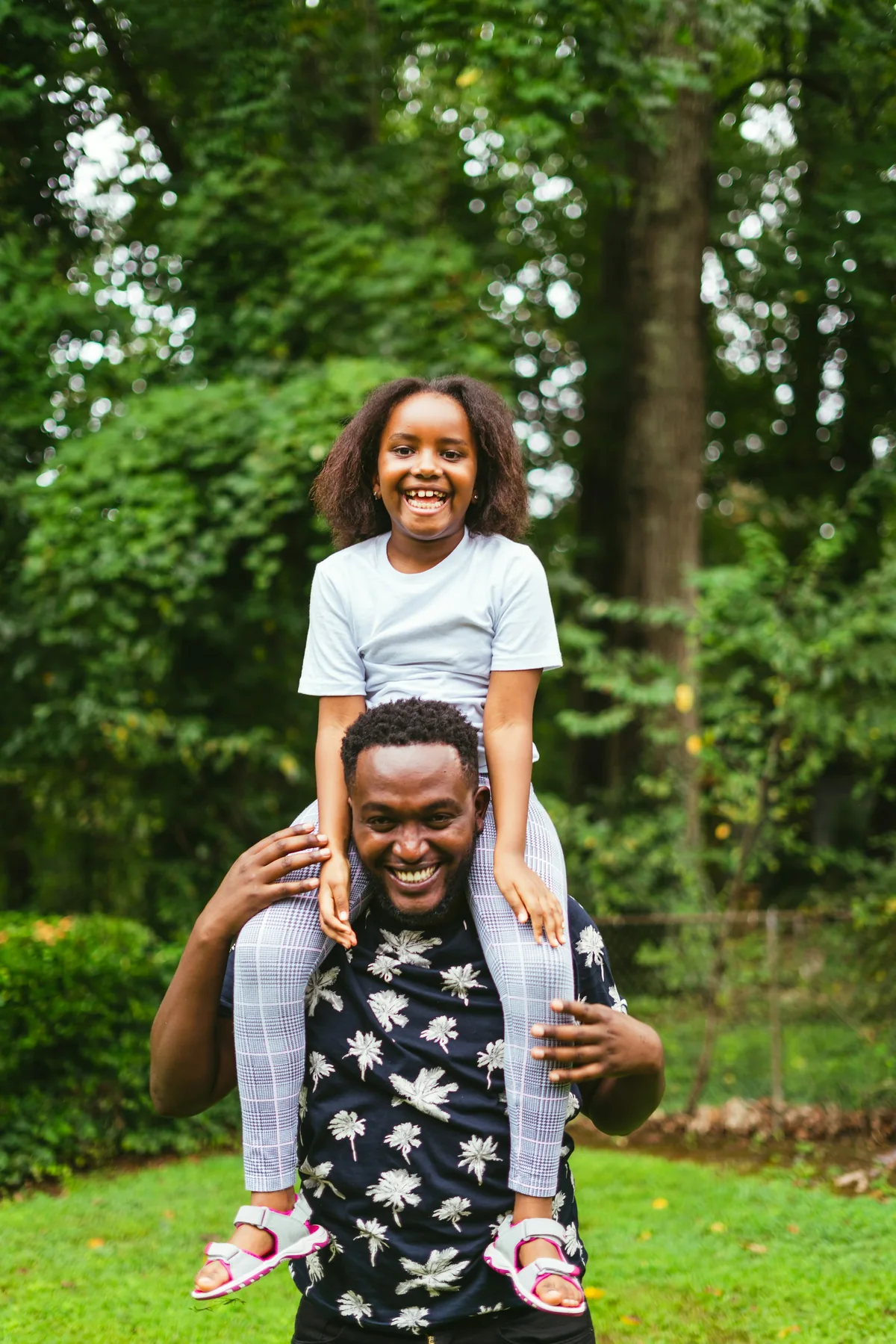 A father carrying his smiling daughter on his shoulders in a green park