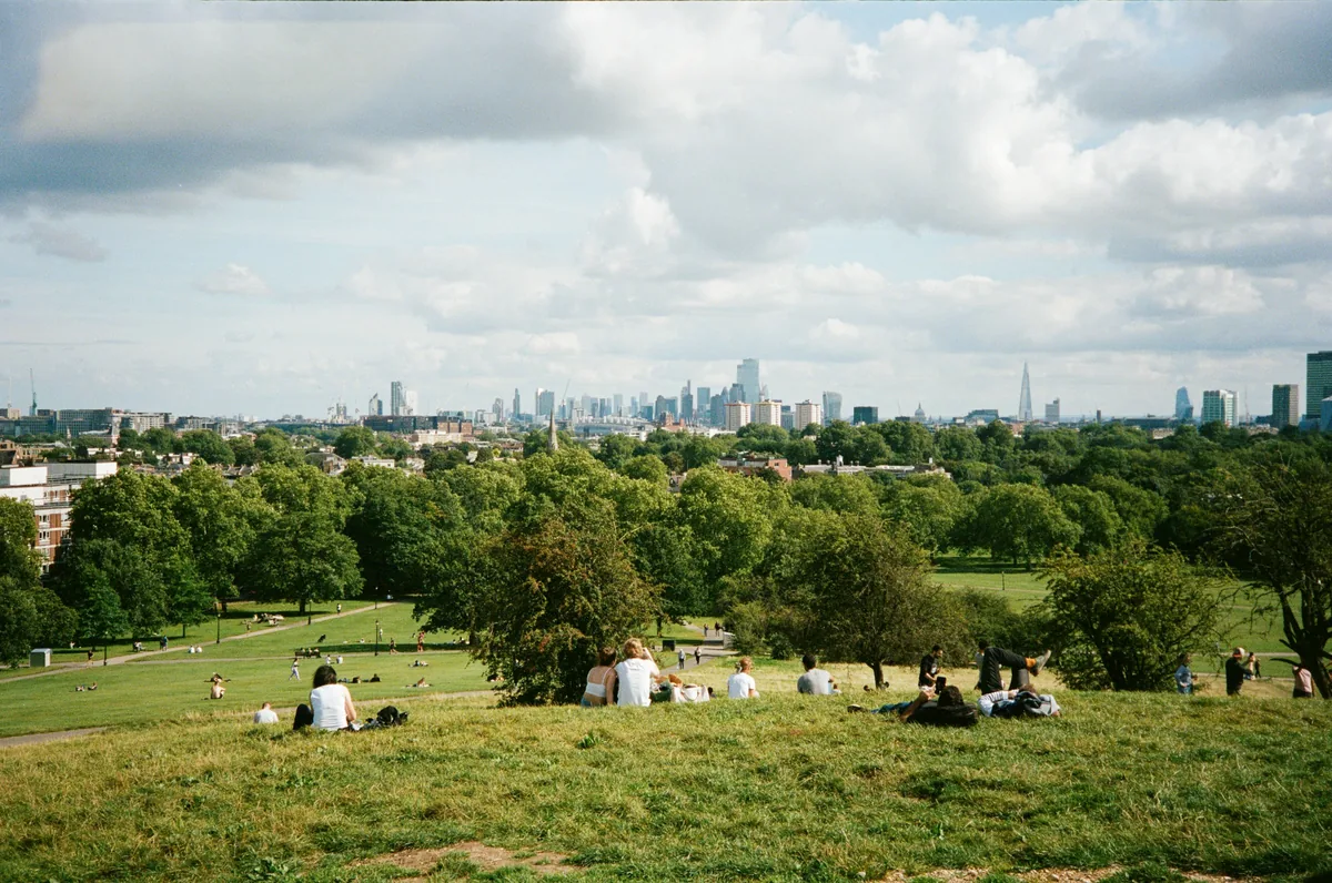 People relaxing on a hillside park above the London skyline